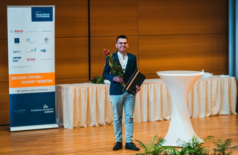 Foto des Preisträgers mit Urkunde und Blumen.