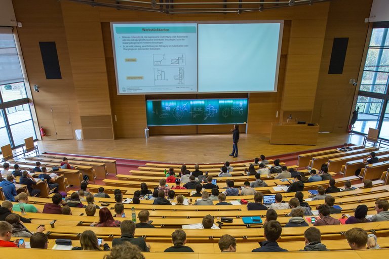 Lecture hall with rows of students, lecturer and blackboard during a lecture.