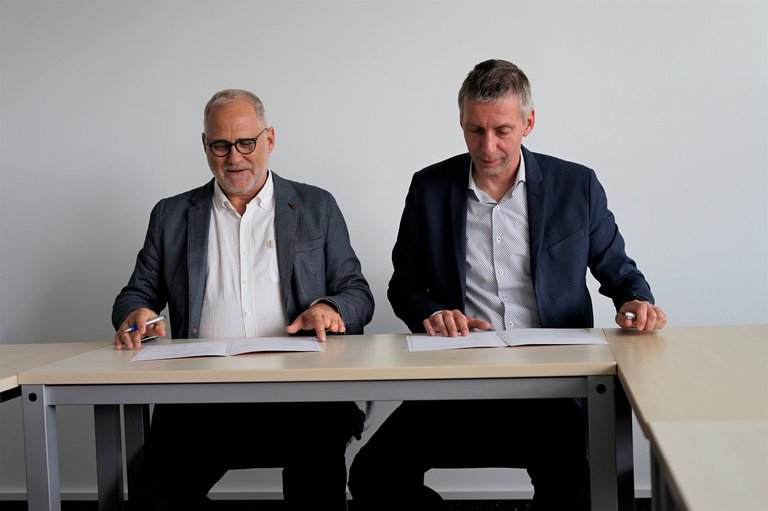 Zwei Personen am Tisch sitzend unterzeichnen jeder ein Papier