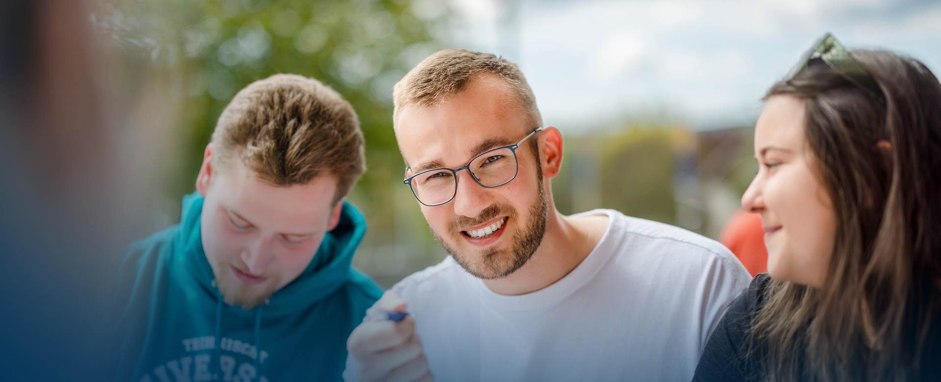 Drei Studierende in Nahaufnahme, einer lächelt in die Kamera