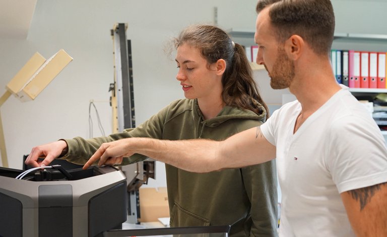 Mann erklärt Schülerin 3D-Drucker