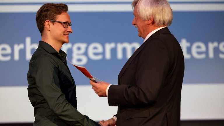 Mann mit Urkunde in der Hand gratuliert anderem Mann