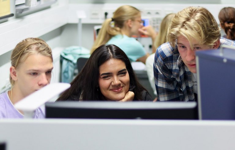 Zwei Schüler am Computer, in der Mitte eine lächelnde Schülerin